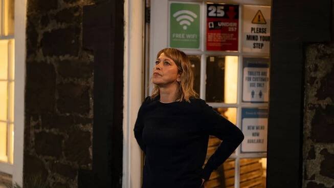 Annika outside of a pub, gazing ahead, looking troubled.