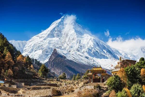 A giant snowy mountain soars above a small village with Buddhist shrines.