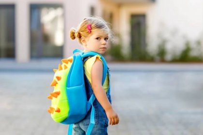 Cute little adorable toddler girl on her first day going to playschool. Healthy upset sad baby walking to nursery school. Fear of kindergarten. Unhappy child with backpack on the city street, outdoors