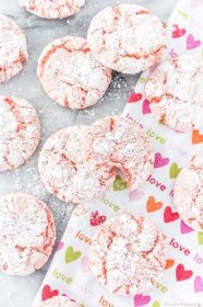 a valentine's day tea towel with strawberry crinkle cookies on top and around it; one of the cookies has a bite out of it.