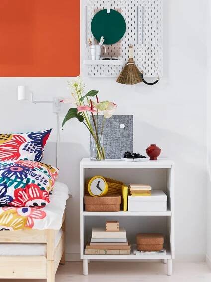 IKEA SKÅDIS white pegboard holding decorations and PLATSA white shelving unit being used as a bedside table.
