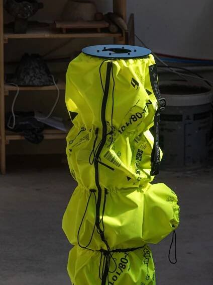 A bright yellow cylindrical object with black markings and a top plate, positioned in a workshop with various tools in the background.