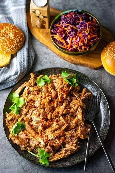 BBQ pulled pork made in a slow cooker on a black plate with a side of red cabbage slaw. 