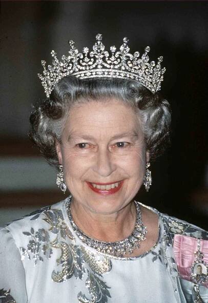 Queen Elizabeth II smiling while wearing a tiara with a ruby and diamond flower motif
