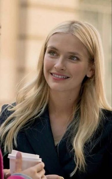 a woman with long blonde hair is smiling and holding a small cup in her hand