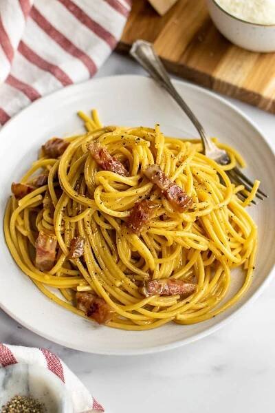 Plate with Bucatini alla carbonara and a striped dish bowl on the side.