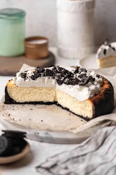 A cheesecake with whipped cream and Oreos on a marble serving platter.