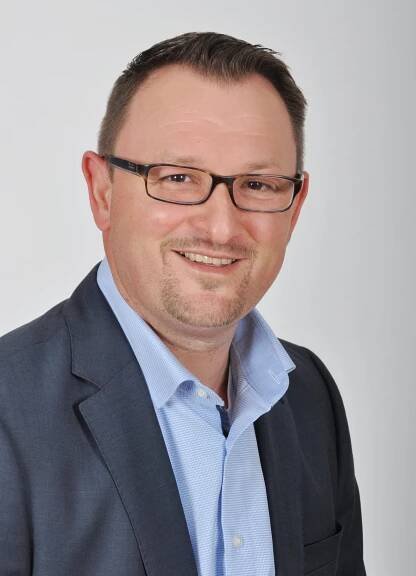 Ein auf Immobilien spezialisierter Mann mit Brille und blauem Hemd.