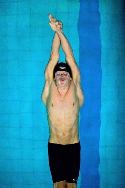 A competitive swimmer in black swimwear stretches upward against a bright turquoise pool background.