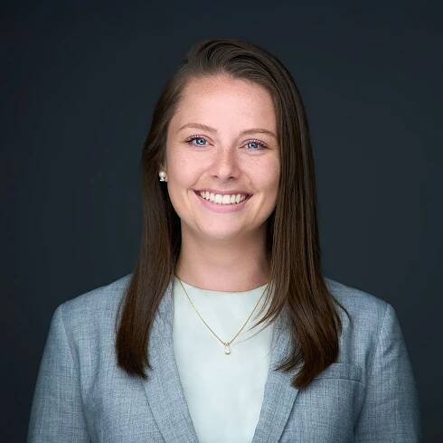 A woman in a suit and necklace is smiling for the camera.