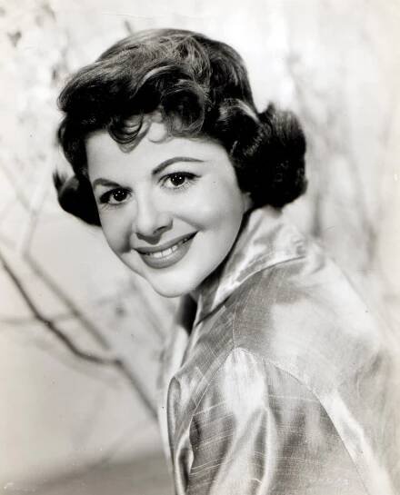 A black-and-white publicity photo of Mitzi McCall, a young woman with dark hair. She looks directly at the camera and smiles.
