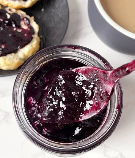 Close-up of a spoonful of blueberry jam over a glass jar.