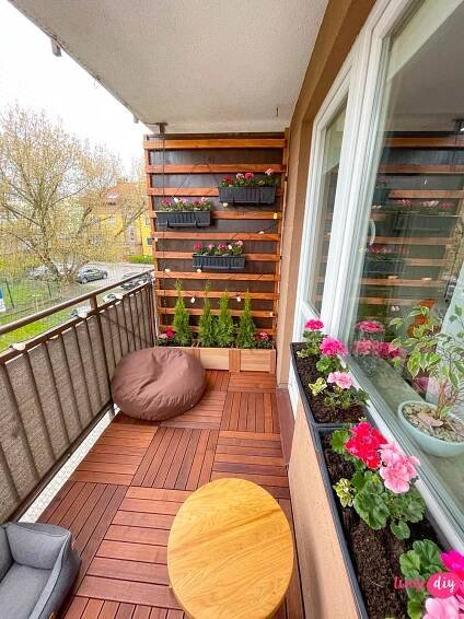 a balcony with potted plants and flowers on the floor next to a table that has a chair