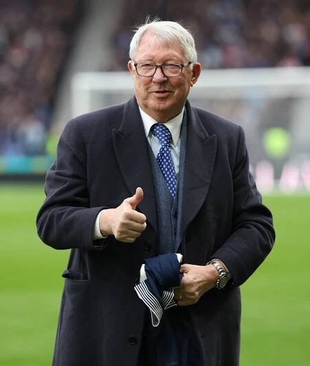 Alex Ferguson giving a thumbs up while holding a jersey.