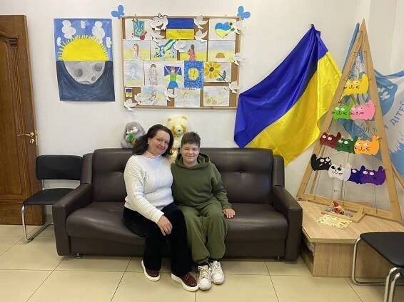 Olena and Misha sitting on a couch, surrounded by drawings and art in the colors of Ukraine's flag.
