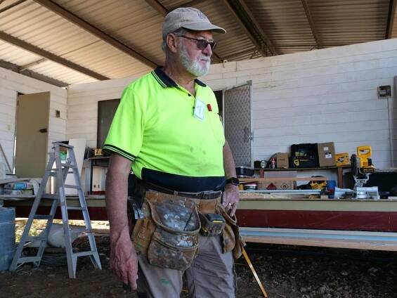 Chris Jacobs standing in a fluoro shirt with a tool belt and hand on his hip.