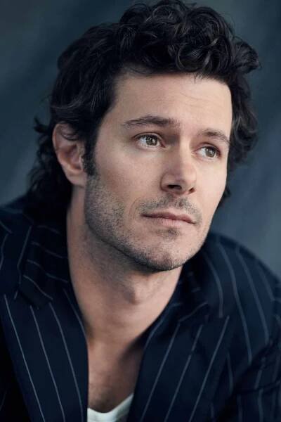 Adam Brody sitting on a chair in a pinstripe suit in a studio