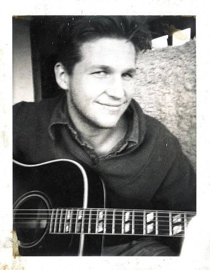 A young Jeff Bridges, smiling slyly and holding a guitar