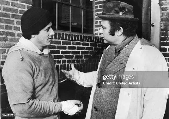 American actors Sylvester Stallone , wearing training clothes, and Burt Young talk outdoors in a still from the film, 'Rocky,' directed by John G....