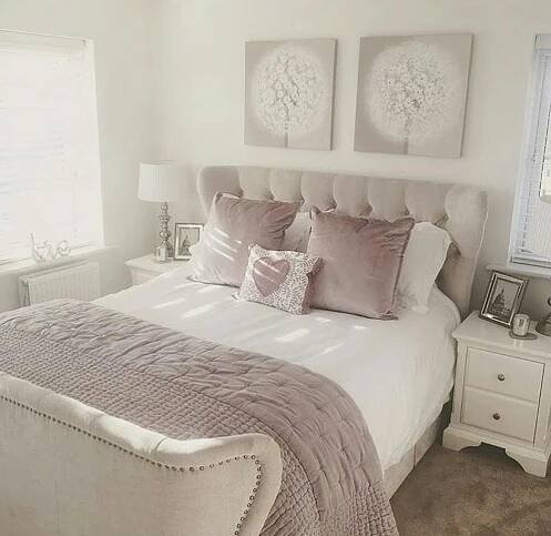 a white bed sitting next to two windows with pink pillows on top of it and an upholstered headboard