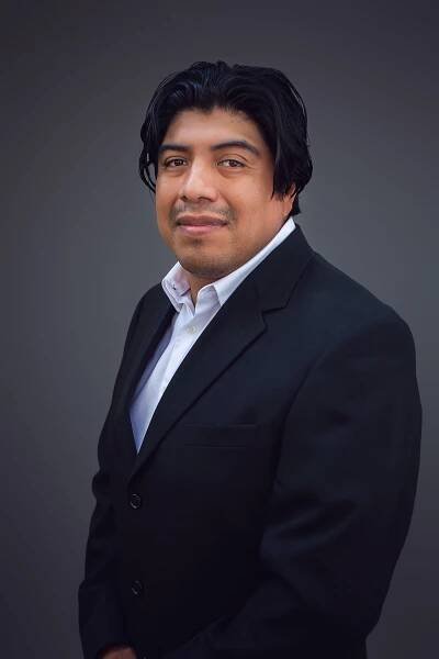 A man in a suit and white shirt is standing in front of a gray background.