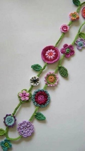crocheted flowers and leaves are arranged on a white surface, with green stems in the center