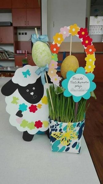 a table topped with a vase filled with fake grass and paper sheep cutouts on top of it