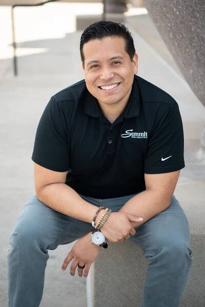 Professional headshot of person in black Nike polo shirt sitting casually outdoors.