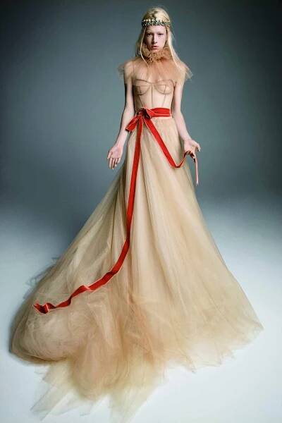 Model in a nude tulle A-line spaghetti strap dress with a corset bodice accented with a red ribbon at the waist