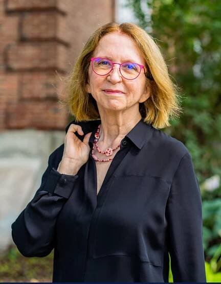 Mid-length blond hair woman closed smile with red glasses.