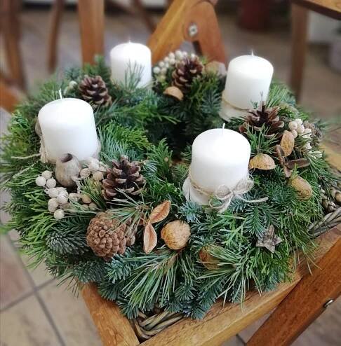 a wreath with pine cones and candles is sitting on a wooden chair in front of a table