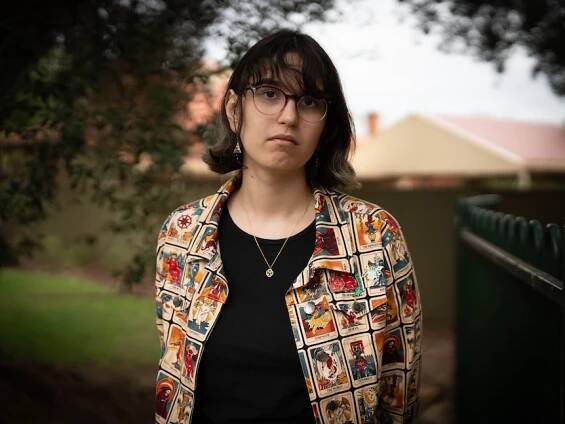 Rowan De Silva looks ahead while standing in a garden area next to a green fence and with housing behind 