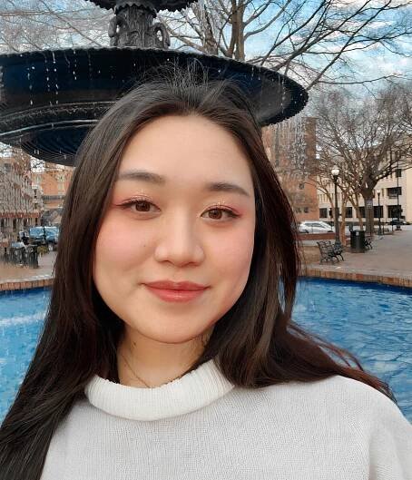 An Asian woman with a white sweater sitting in front of a fountain