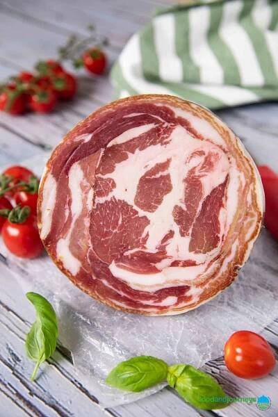 An image of a rolled pancetta with cherry tomatoes in the background.