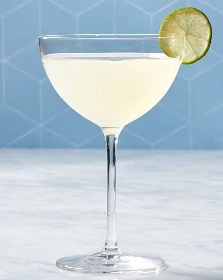 a classic daiquiri cocktail in a coupe glass with a lime garnish against a blue backdrop