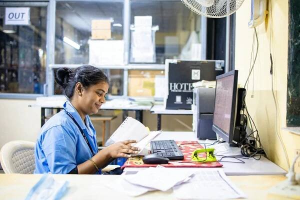 Free A woman in an office setting reading paperwork at her desk with a computer. Stock Photo