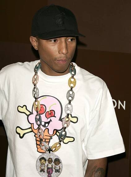 Pharrell wearing an ice cream shirt with large chain and black hat.