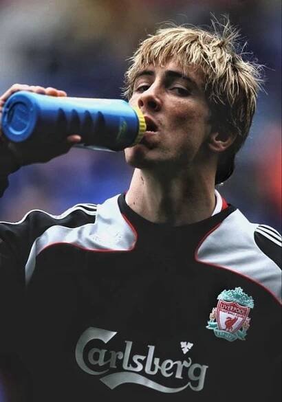 a young man drinking from a blue and black bottle while standing on a soccer field