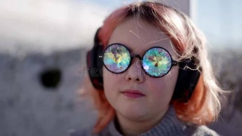Preteen girl is enjoying music by headphones on street, portrait of child with funny glasses