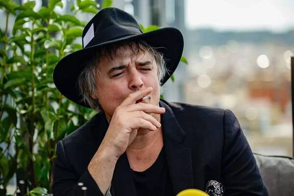 Head and shoulders image of rock star Pete Doherty, wearing a black fedora hat and suit jacket, smoking a cigarette during a press event in Spain. He is promoting his film there.