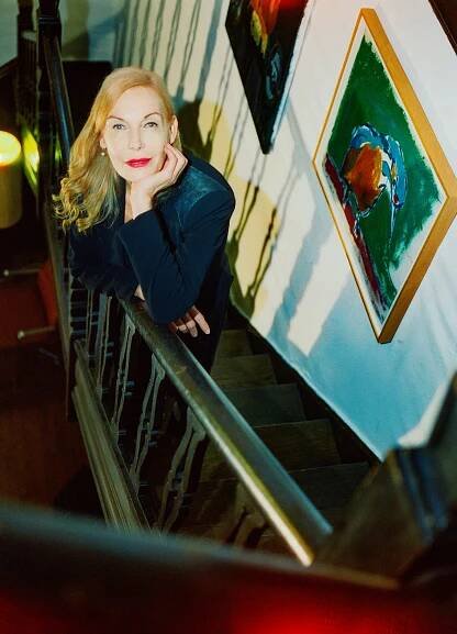Lemper, posing for a portrait on a staircase of the Birdsong Society, with a brightly colored painting of a bird on the wall beside her.