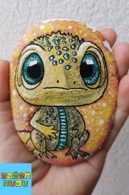 a hand holding a rock with a lizard painted on it's face and eyes