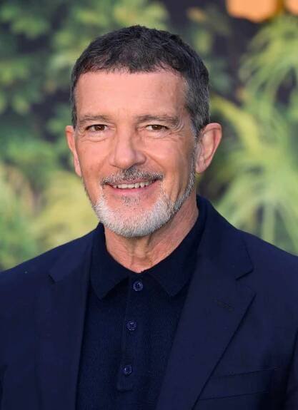 Antonio Banderas with dark gray hair and a gray beard wearing a navy blazer over a matching polo