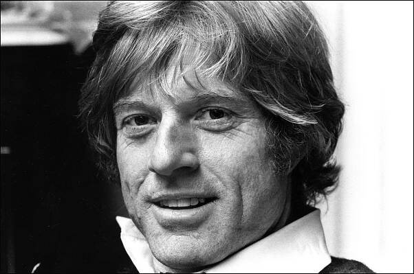 A black and white, close-up picture of Robert Redford smiling.