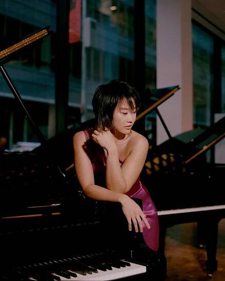 Yuja Wang is shown posing in a piano showroom, leaning against a Steinway.