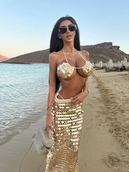 Woman in gold sequined bikini and skirt on a beach.