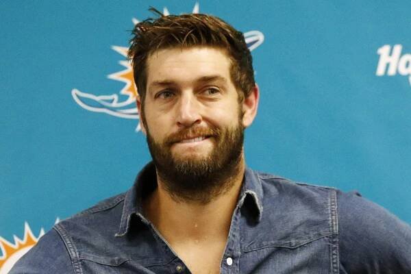 Jay Cutler wears a blue denim shirt and smiles during a postgame news conference in front of a Miami Dolphins backdrop