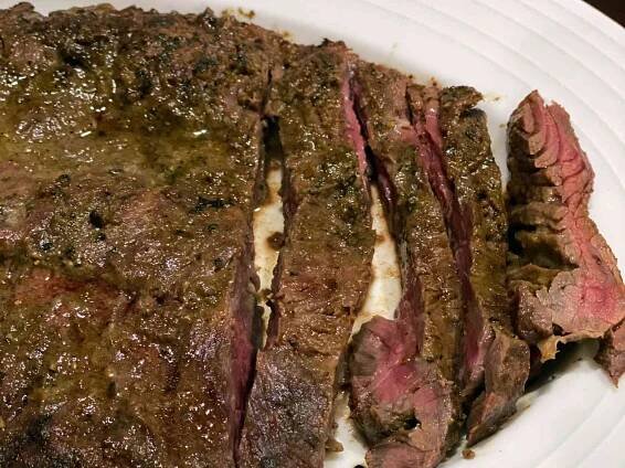 closeup of Chef John's Grilled Flap Steak, partially sliced to show the pink interior, on a white serving platter