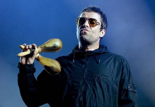 Liam Gallagher performing at a concert, holding maracas.