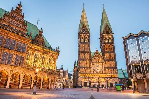 Der Marktplatz in Bremen mit dem historischen Rathaus und der beeindruckenden St. Petri-Dom-Kirche im Hintergrund, beleuchtet in der Dämmerung.